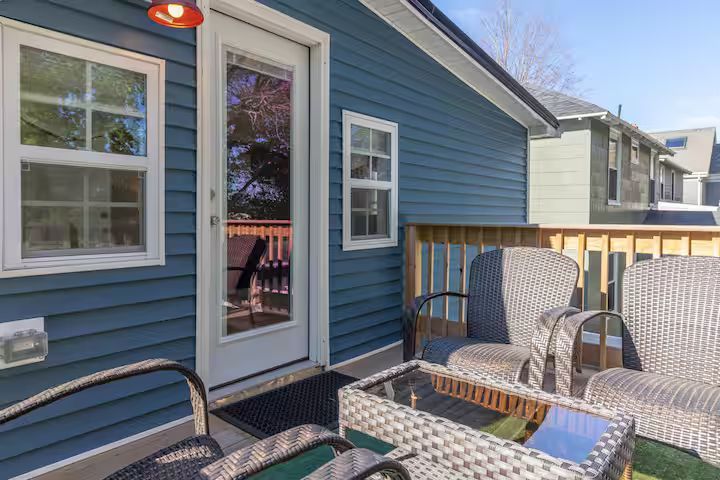 Small patio with blue siding, wicker chairs, and a glass-top table beside a sliding door.