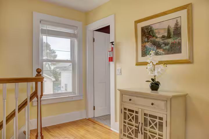 Bright hallway with wooden stairs, a window, open door, and beige cabinet with floral painting