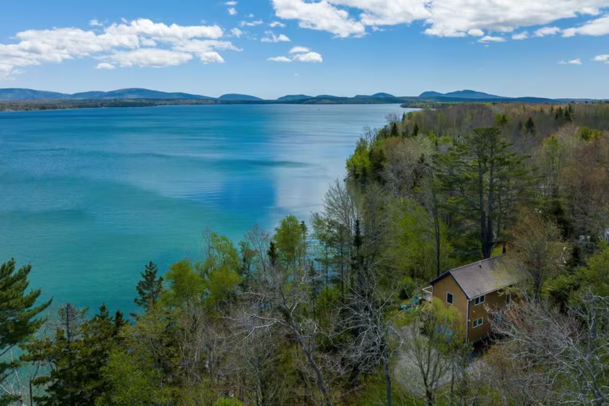 Turquoise lake beside a wooded shoreline with a small cabin under a blue sky