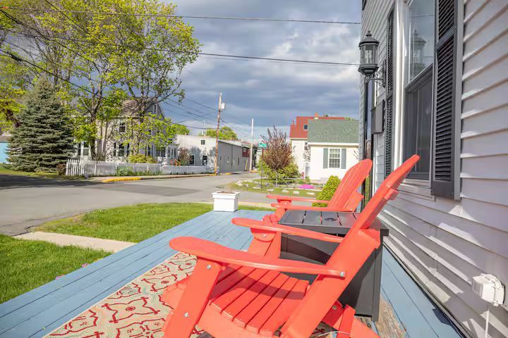 Red Adirondack chairs on a porch beside a quiet neighborhood street on a sunny day