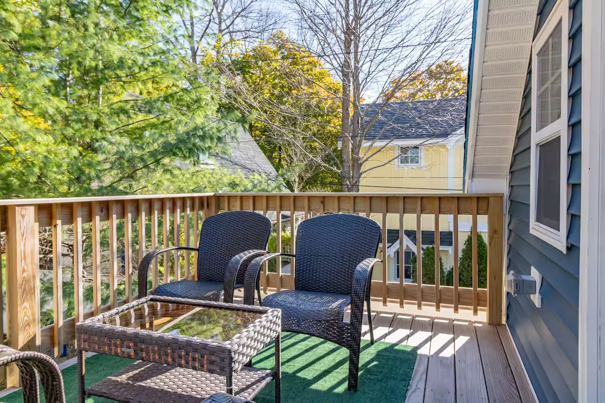 Wooden deck with two black chairs and a small table overlooking a leafy backyard