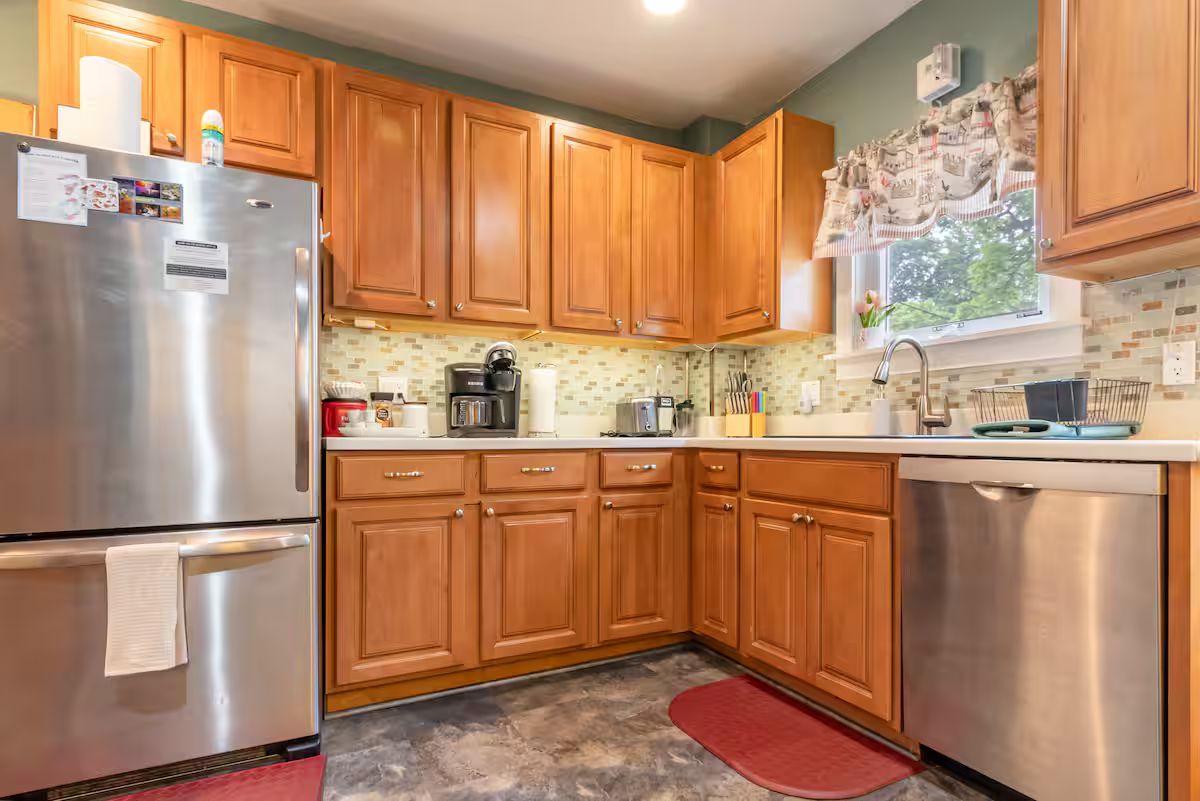 Compact kitchen with stainless steel appliances, wooden cabinets, and a tiled backsplash.