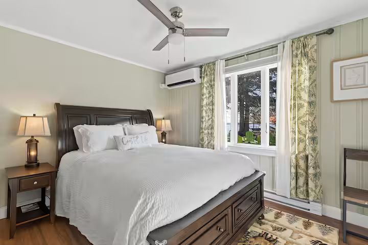 Bright bedroom with a bed, nightstand lamp, ceiling fan, and window with floral curtains.