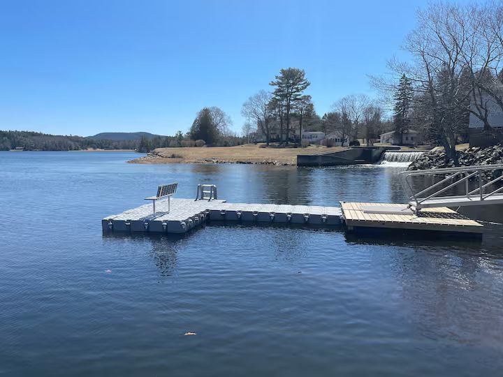 Snow-dusted lakeside dock on a calm blue lake under a clear sky
