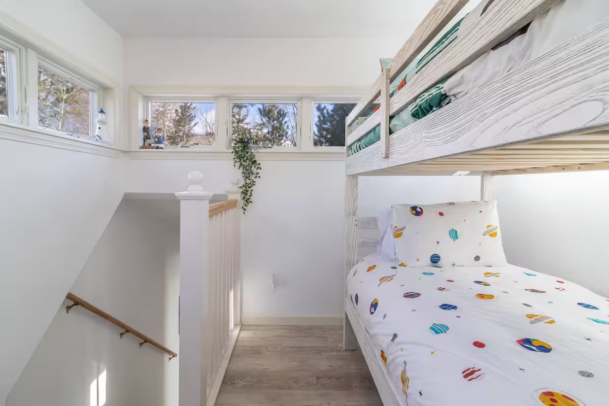 Bright white loft bedroom with a bunk bed, small windows, and a staircase railing.