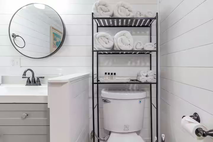 Small bathroom with black shelving, white towels, sink, mirror, and toilet paper holder