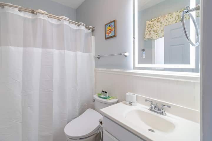 Small white bathroom with shower curtain, toilet, sink, and bright vanity mirror