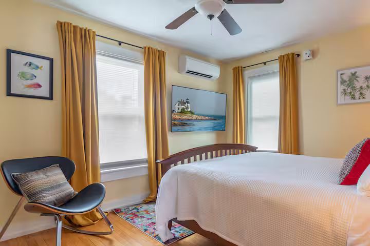 Bright bedroom with bed, chair, windows, wall art, and ceiling fan