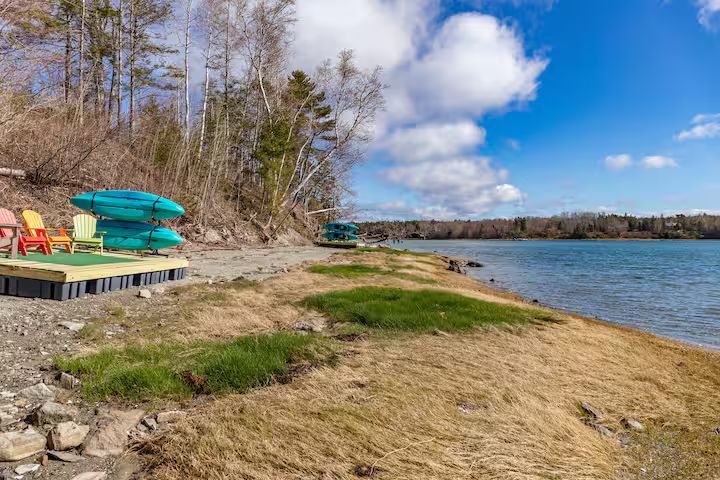 Kayaks stacked on a dock beside a rocky lakeshore under a blue sky