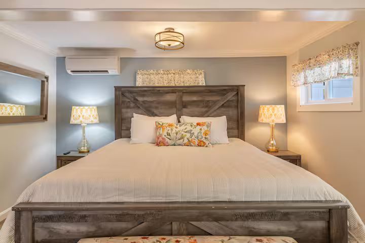 Cozy bedroom with a wooden bed, floral pillows, bedside lamps, and light gray walls