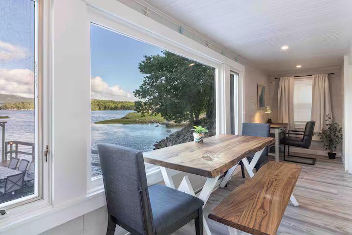 Bright lakeside dining area with white table, wooden benches, and open view to water through large windows