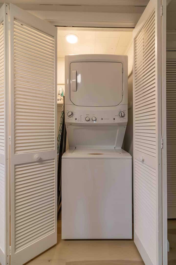 Stacked washer and dryer in a white laundry closet with louvered doors open