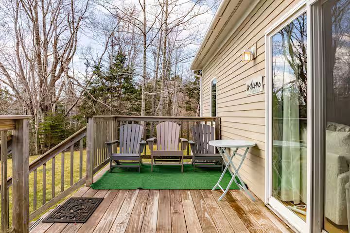 Wooden backyard deck with two chairs, small table, and sliding glass door beside a house