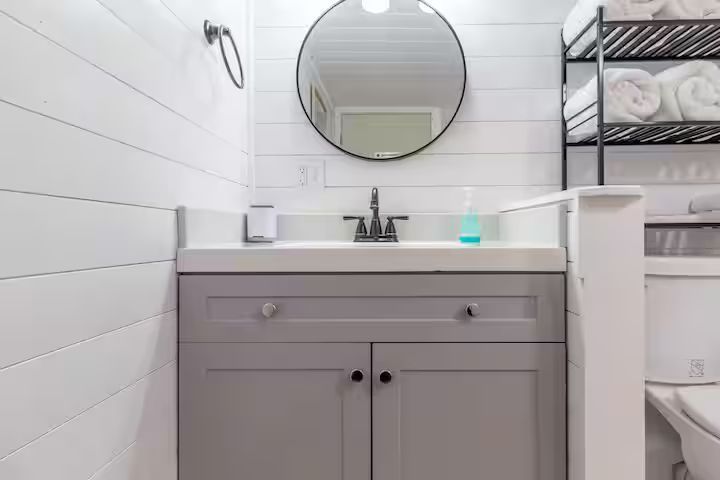 Small bathroom vanity with round mirror, sink, and white tile walls