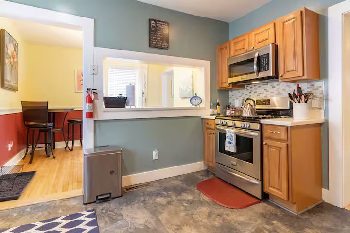 Compact kitchen with wood cabinets, stainless steel appliances, and a pass-through opening to another room.
