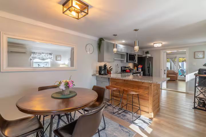 Bright open kitchen and dining area with round table, island stools, and hardwood floors