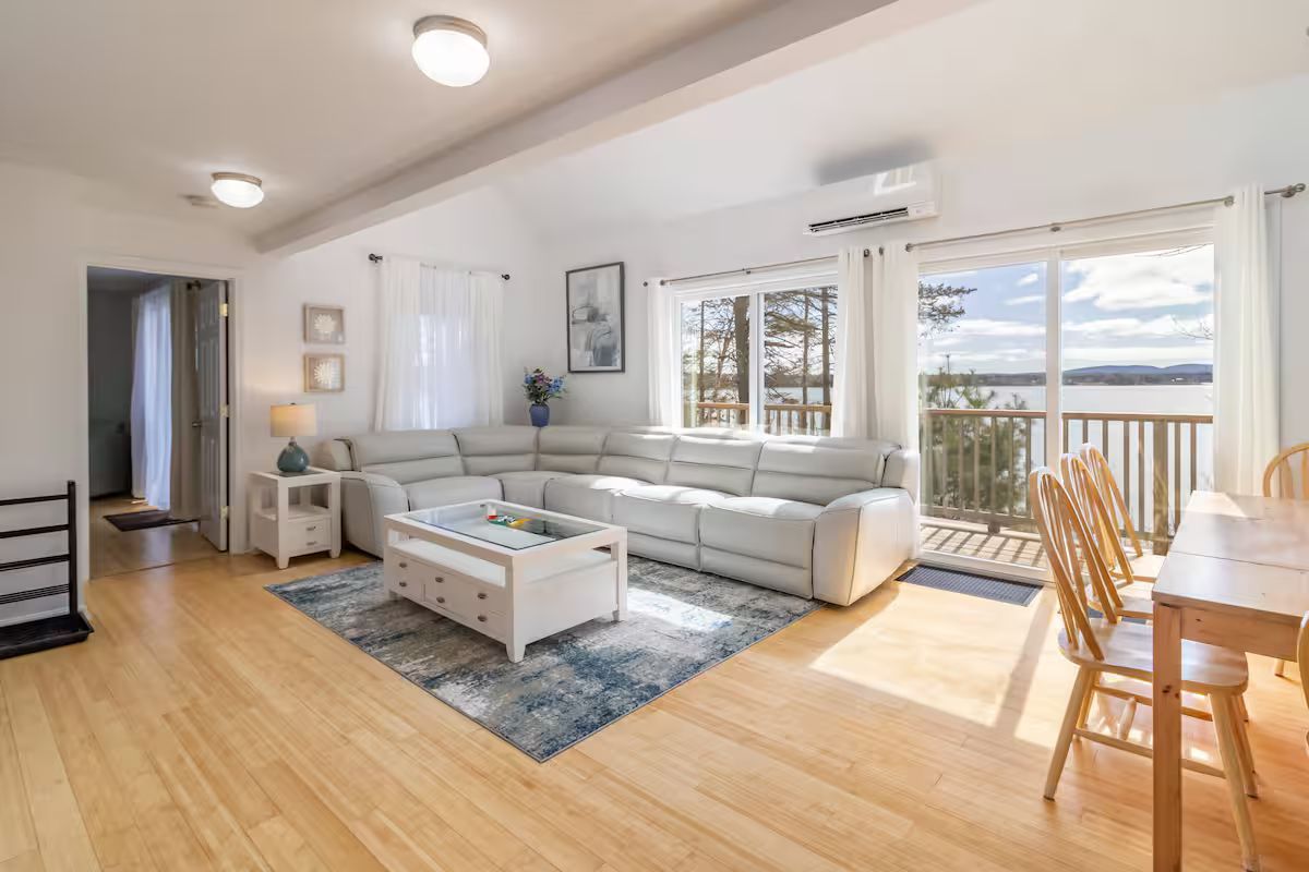 Bright open living room with sectional sofa, coffee table, wood floors, and sunlight through balcony doors
