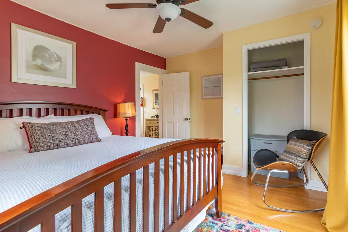 Cozy bedroom with wood bed, red accent wall, ceiling fan, open closet, and yellow curtains