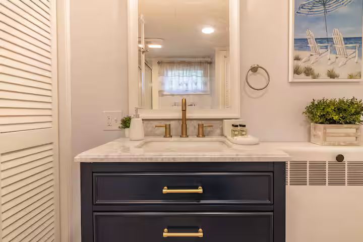 Modern bathroom vanity with navy drawers, white marble countertop, brass faucet, and seaside wall art