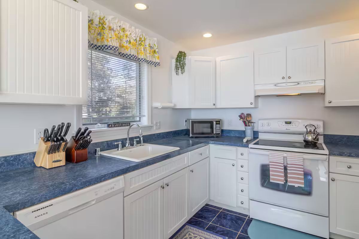 Bright white kitchen with blue countertops, white cabinets, and a window over the sink