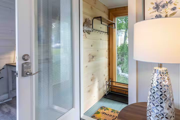 Small entryway with a frosted glass door, wall hooks, and a lamp on a table by a window.