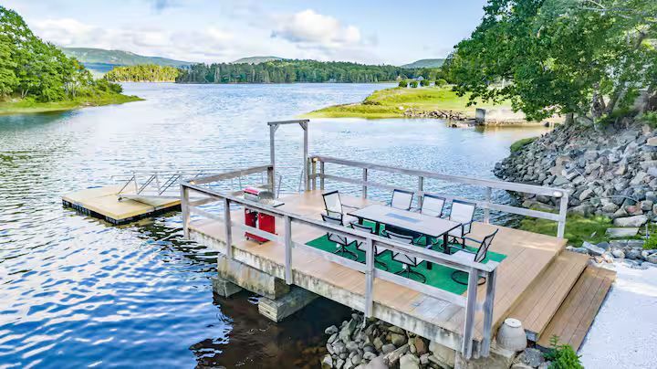 Wooden dock on a calm lake with green hills and rocky shore under a bright sky