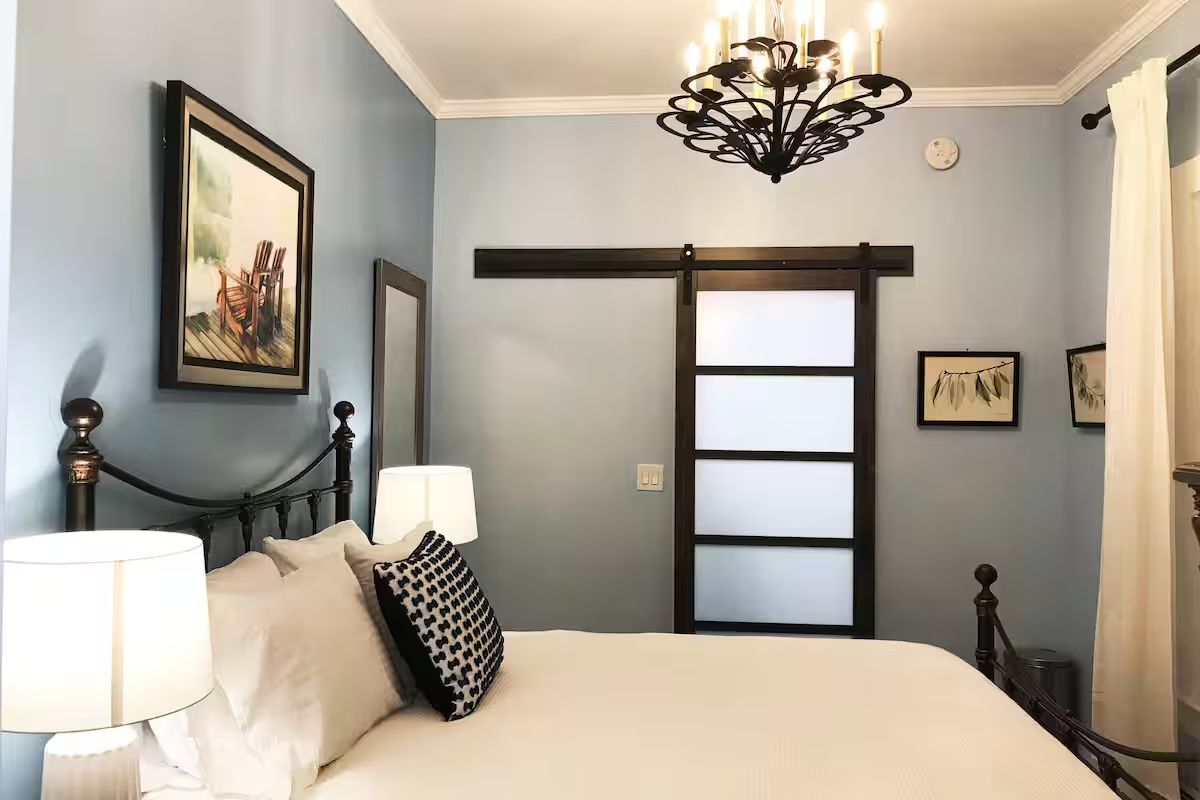 Cozy blue bedroom with white bedding, black metal bed frame, chandelier, and barn-style sliding door
