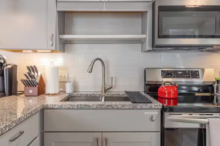Modern kitchen with gray cabinets, stainless steel appliances, and a red kettle on the stove