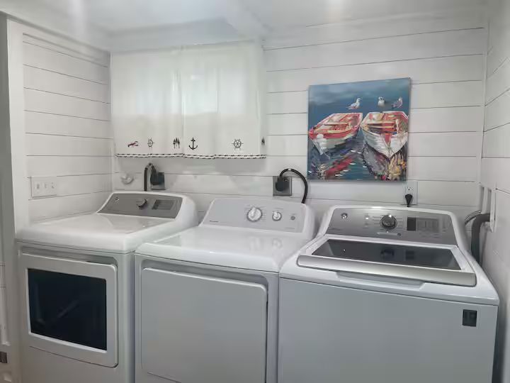 Laundry room with white washer and dryer under a window, plus a sink and wall art above.
