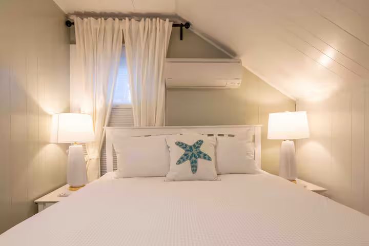 Cozy white bedroom with twin lamps, curtained window, and starfish pillow on a neatly made bed