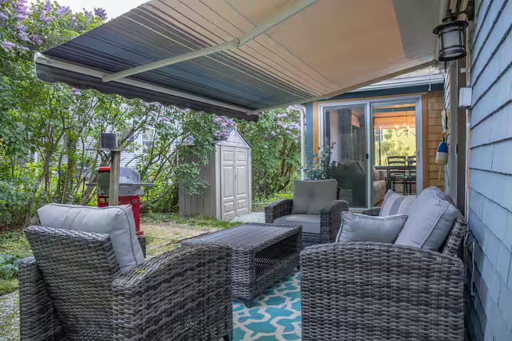 Covered patio with wicker seating, gray cushions, and a striped awning in a backyard garden