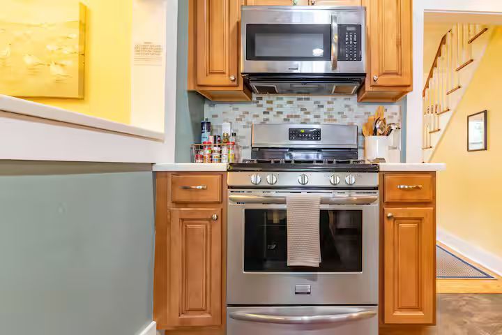 Compact kitchen with stainless steel stove and microwave, wooden cabinets, and tiled backsplash