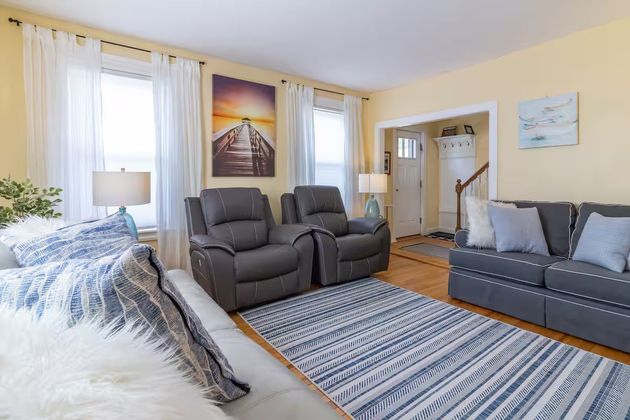 Bright living room with gray recliners, blue sofa, striped rug, and large windows with sheer curtains
