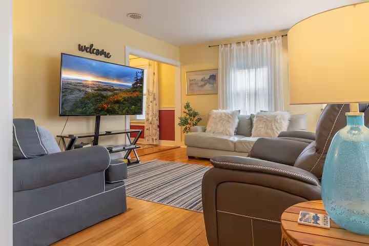 Bright living room with gray sofas, wall-mounted TV, striped rug, and warm lighting