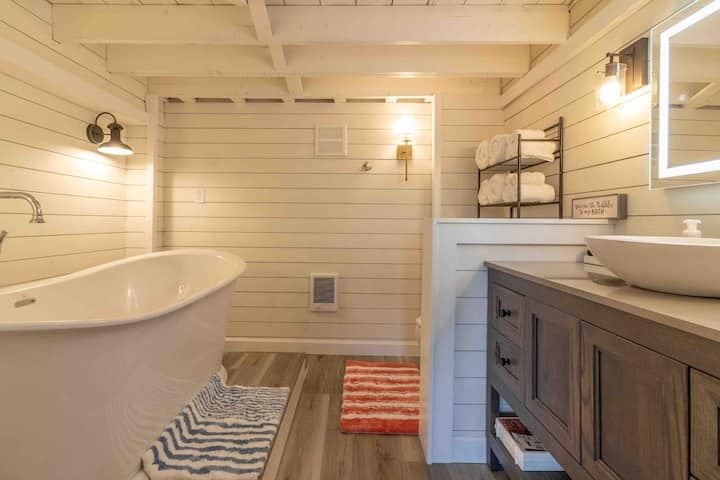 Bright farmhouse bathroom with freestanding tub, wood vanity, striped rugs, and wall sconces
