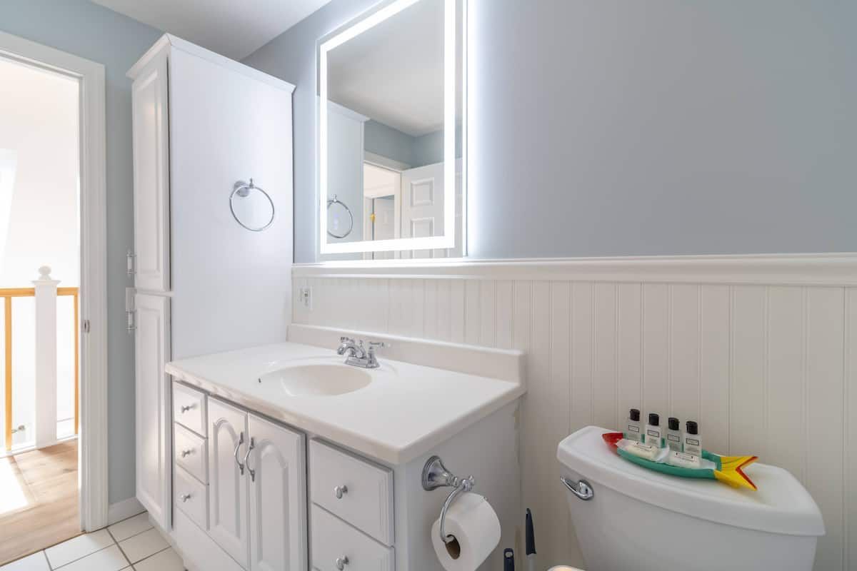 Bright white bathroom with vanity, mirror, and toilet, lit by a window.