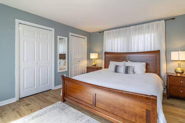 Bright bedroom with a wooden bed, white bedding, gray walls, and two bedside lamps