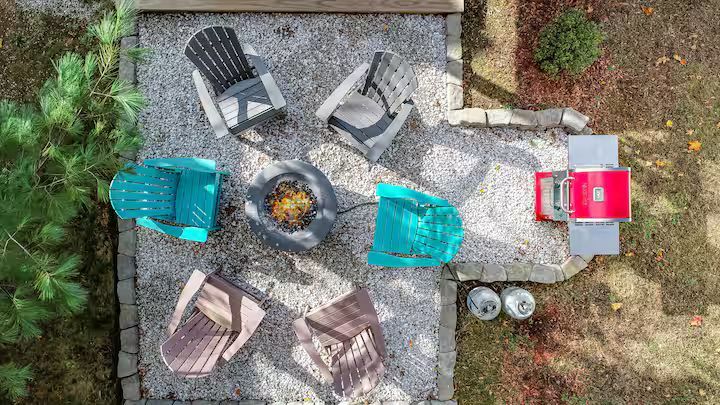 Overhead view of a backyard fire pit with six chairs around it on a stone patio and gravel area