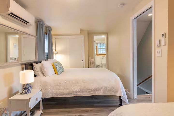 Bright bedroom with a bed, nightstand lamp, air conditioner, and open doorway to a bathroom