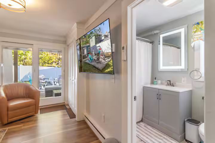 Bright hallway with wall art, tan chair by a window, and a small bathroom vanity at the end.