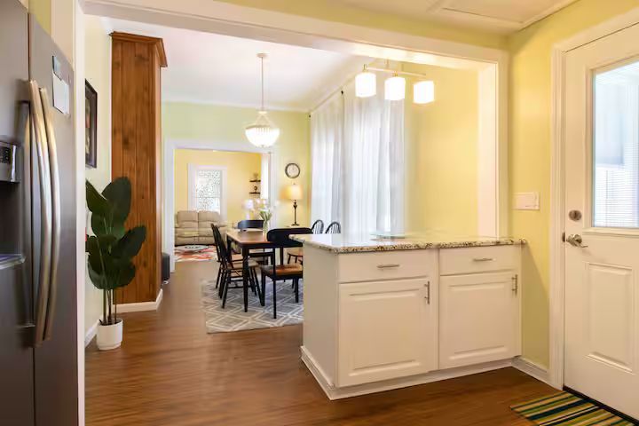 Bright kitchen with white island, wood floors, and dining area beyond a wide doorway