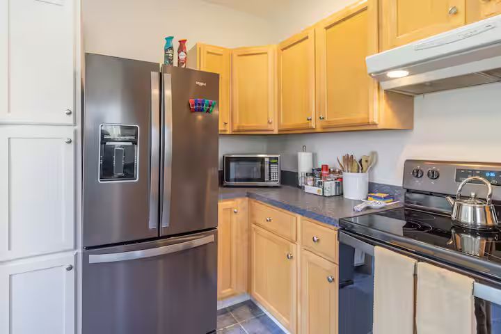Modern kitchen with stainless steel fridge, light wood cabinets, and a stove with a kettle