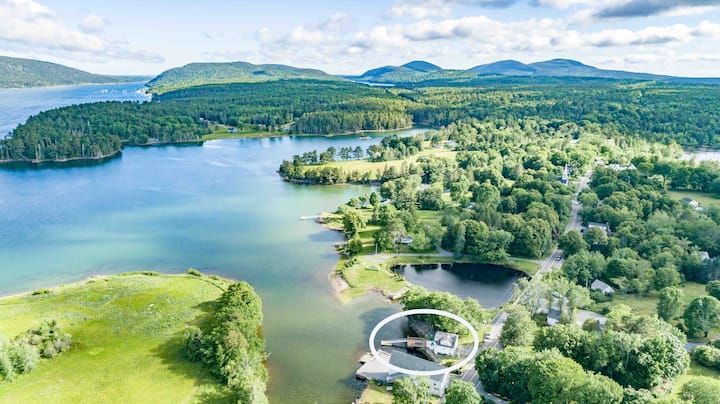 Aerial view of a green lake with forested shores, hills, and a small docked building near the water