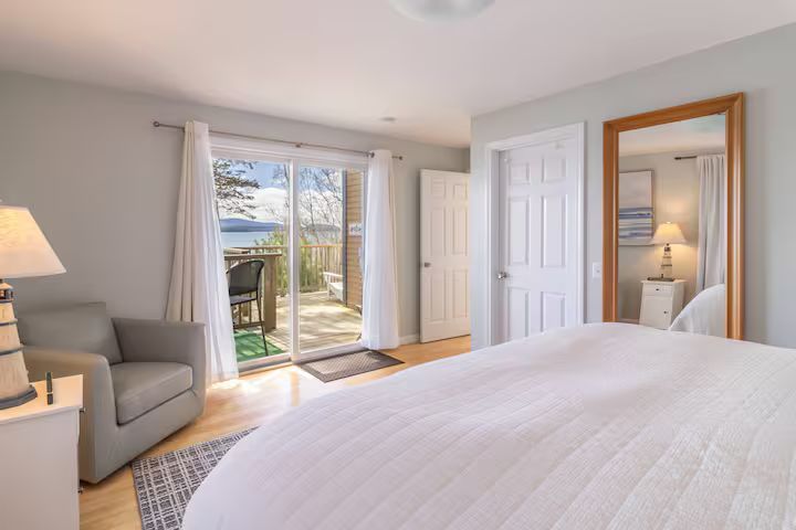 Bright bedroom with a large bed, gray chair, mirror, and sliding glass doors to a balcony.