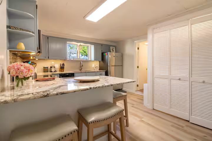 Bright kitchen with white cabinets, marble island, bar stools, and louvered closet doors