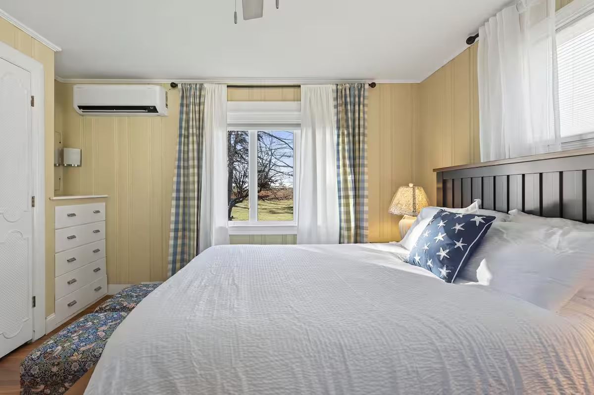 Bright bedroom with a bed, window view, striped wallpaper, white dresser, and lamp