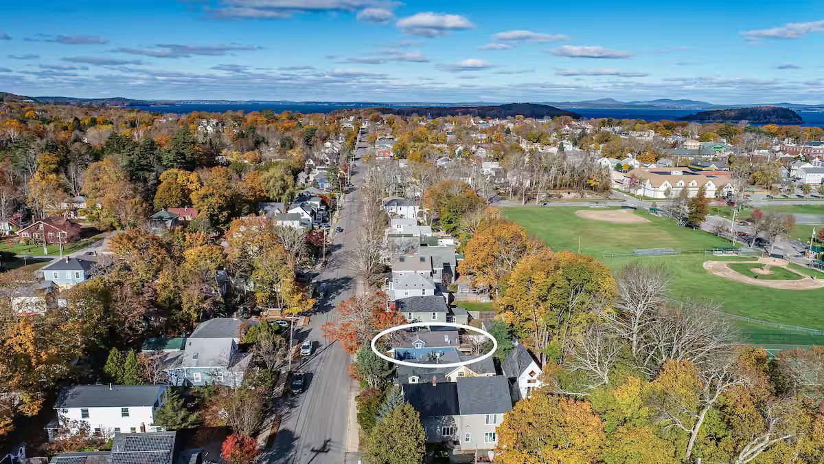 Aerial view of a tree-lined suburban street with autumn foliage and a park on the right.