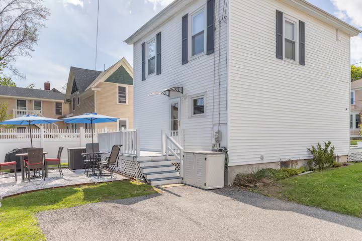 Exterior of a white two-story house with a small patio, stairs, and lawn in a residential neighborhood