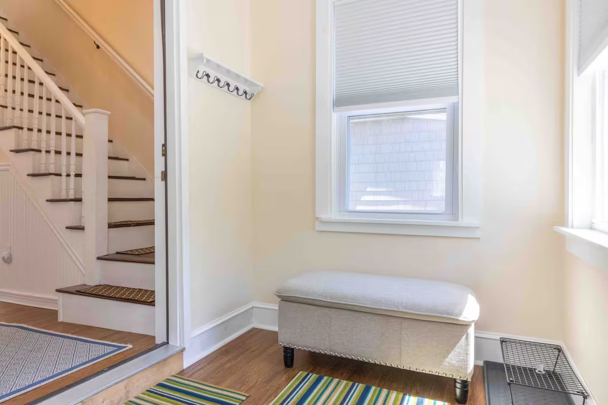 Bright entryway with staircase, window seat, and striped rug in a light-colored hallway