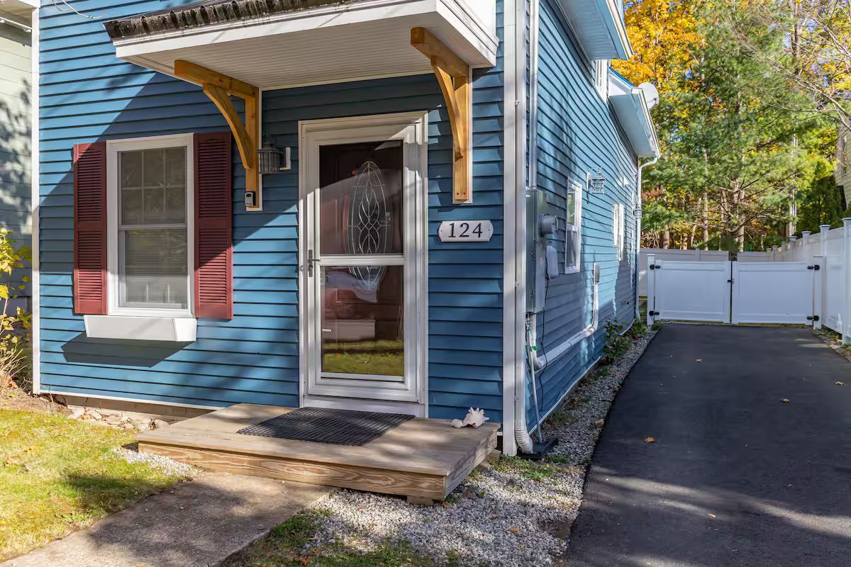 Blue house front entrance with red shutters, small porch, and driveway beside a white fence